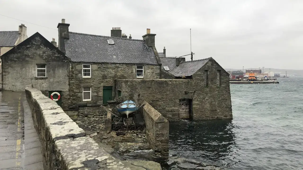 Stenhus vid havet, en blå båt på land. Känns som en scen från en Shetland serie.