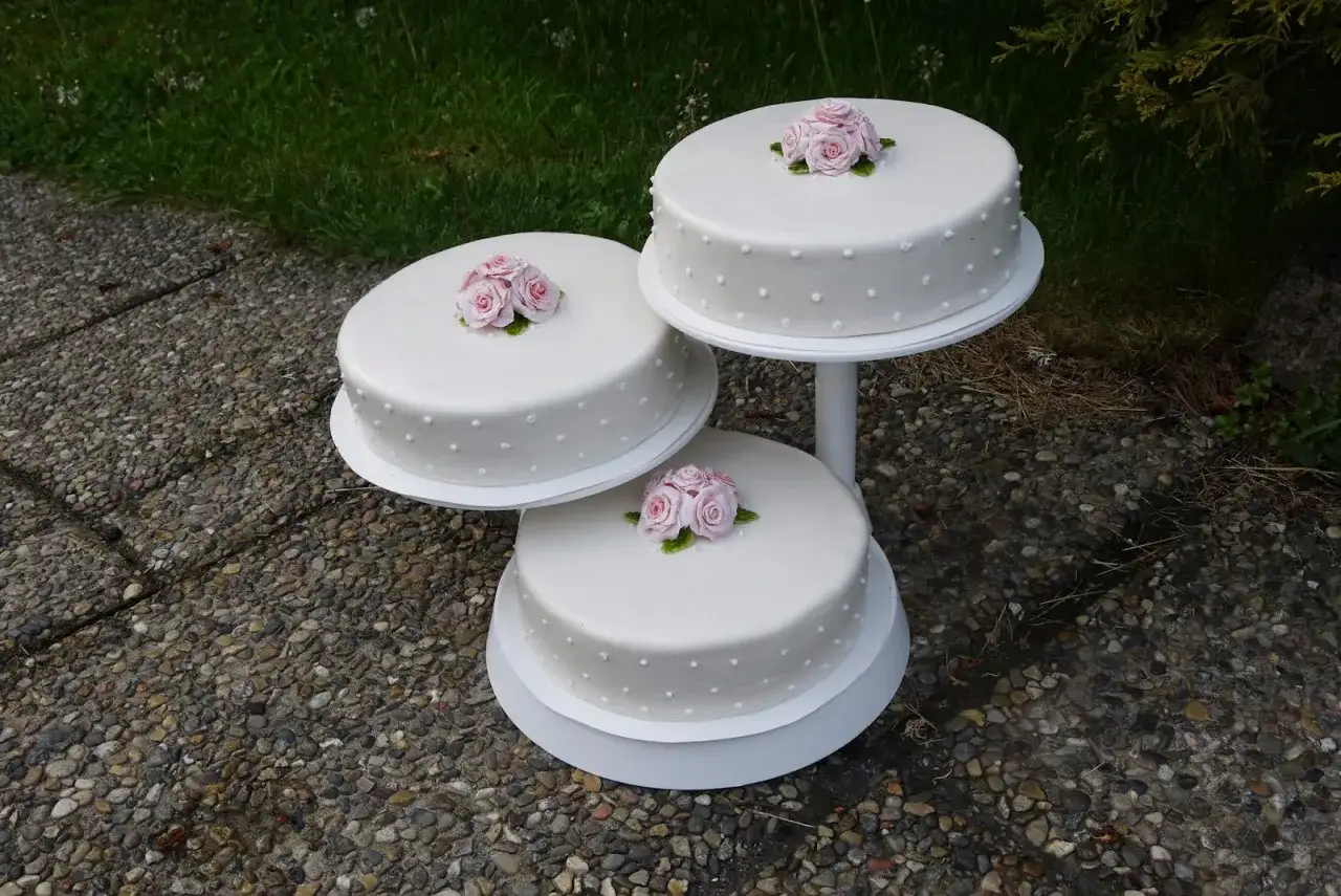 Tre vita tårtor med rosa rosor och chokladdekorationer står på ett tårtfat utomhus.