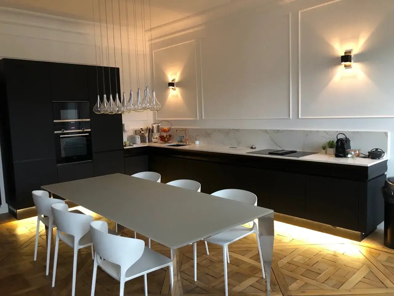 Cuisine moderne et épurée, avec une grande table blanche et des chaises assorties. L'absence de hotte visible renforce le design minimaliste.