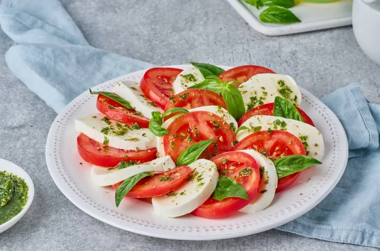 Sałatka Caprese z pomidorów i mozzarelli, posypana ziołami. Bazylia do czego dodawać? Do tej pysznej sałatki!
