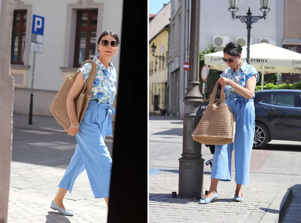Letnia stylizacja: błękitne spodnie kuloty z wiązaniem w pasie, kwiecista bluzka i pleciona torba.