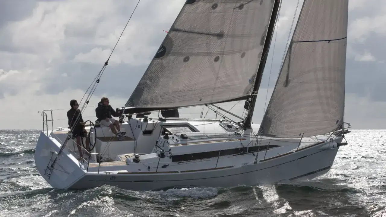 Deux hommes naviguent sur un voilier blanc par temps venteux. Le bateau, un modèle 35, fend les vagues sous un ciel nuageux.