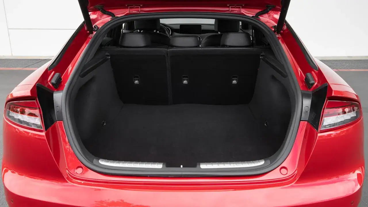 Maletero abierto de un Kia Stinger rojo, mostrando su amplio espacio interior y asientos traseros plegables.