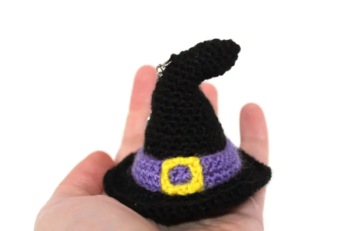 Sombrero de bruja amigurumi negro con cinturón morado y hebilla amarilla. ¡Un patrón gratis para crear tu propia magia!