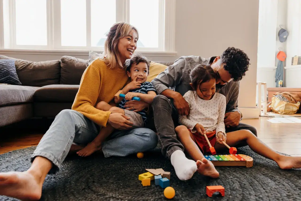 Eine Familie spielt mit Bauklötzen und einem Xylophon. Die Eltern lachen und machen ihren Kindern eine Freude.