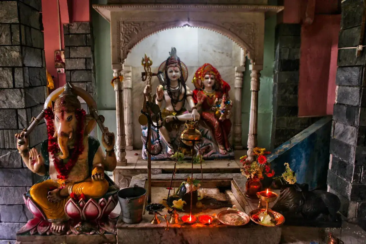 En hinduisk gud, Ganesha, sitter framf&ouml;r en helgedom med Shiva och Parvati. Ljus brinner och blommor pryder altaret.