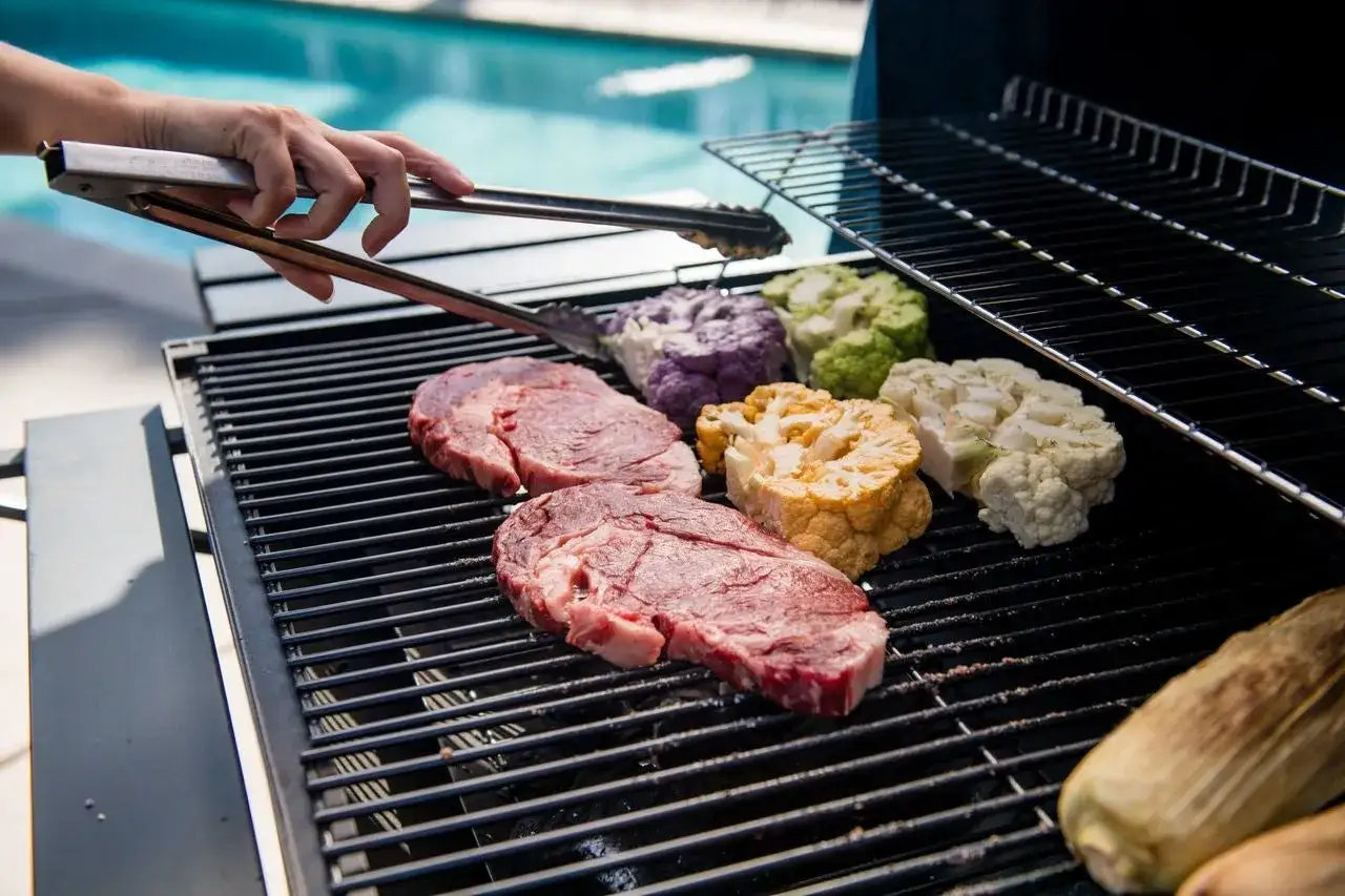 Deux steaks de viande à faire au barbecue, accompagnés de choux-fleurs colorés et d'épis de maïs.
