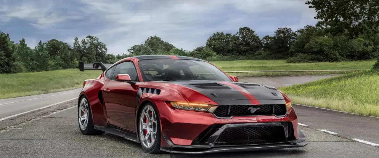Roter Mustang GTD mit schwarzer Motorhaube und roten Streifen auf einer Landstraße, bereit für die Rennstrecke.