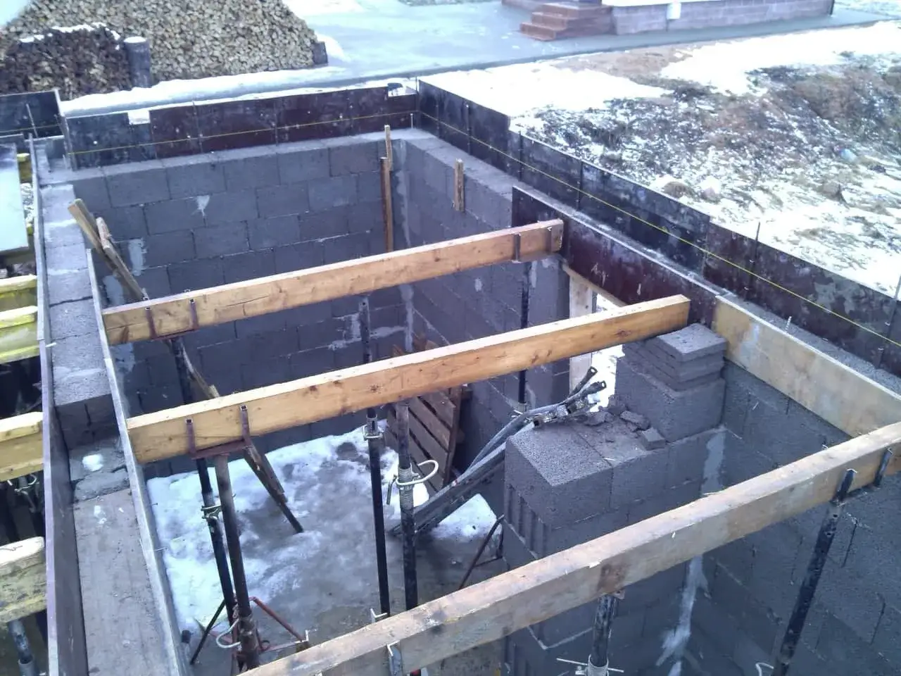 Budowa fundamentów z bloczków betonowych, drewniane belki podtrzymują szalunek. Cena betonu jest kluczowa dla tej inwestycji.