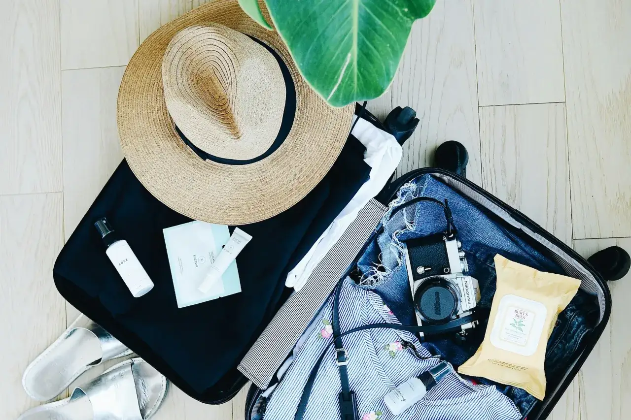 Packliste Wohnmobil: Sonnenhut, Kleidung, Kamera, Kosmetik und silberne Sandalen für die Reise.