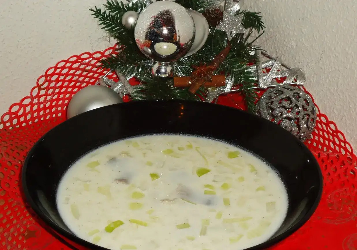 Zupa śledziowa Ani gotuje się w świątecznej atmosferze. Kremowa, z kawałkami śledzia i pora, podana na czerwonym, ażurowym obrusie, w otoczeniu choinkowych ozdób.