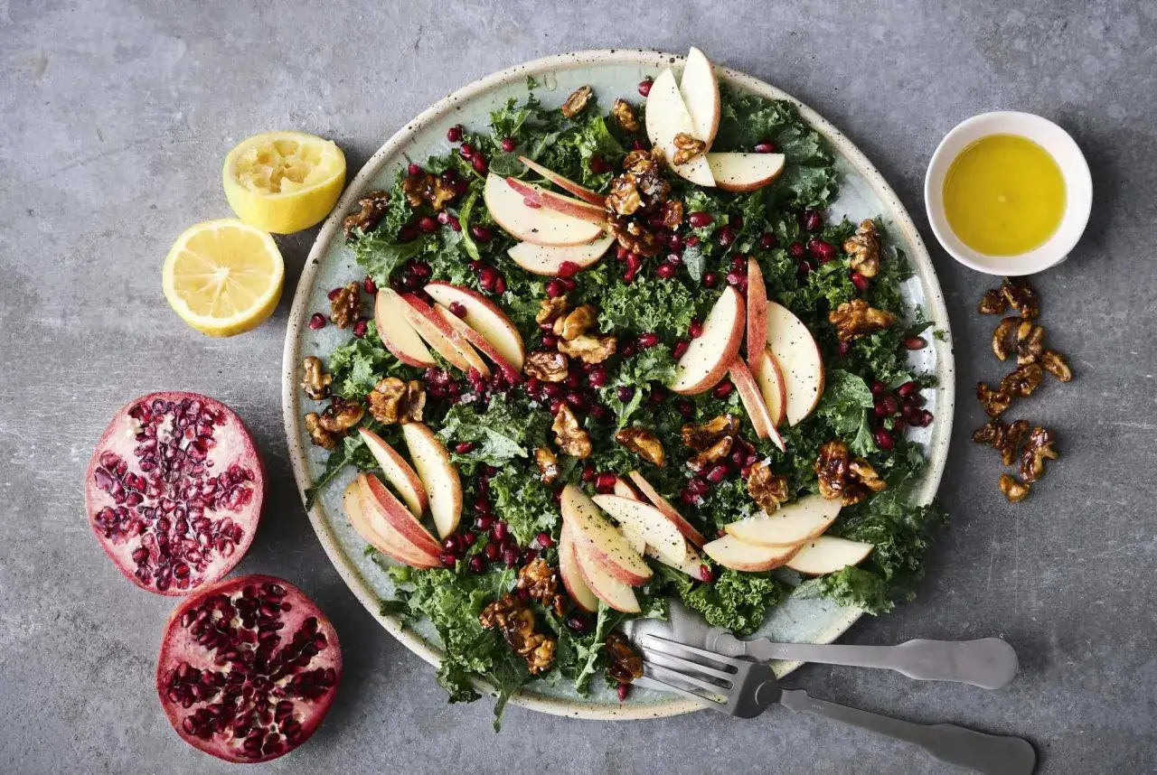 En frisk och f&auml;rgglad gr&ouml;nk&aring;lssallad med &auml;pple, granat&auml;pple och valn&ouml;tter, perfekt som en l&auml;tt sallad till julbordet.