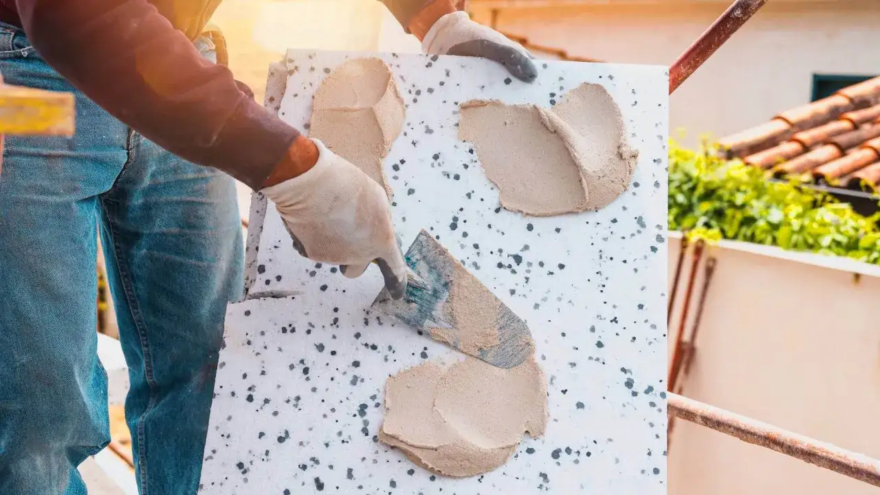 Ręce w rękawiczkach nakładają zaprawę na styropian, pokazując, jak nakładać klej na styropian.