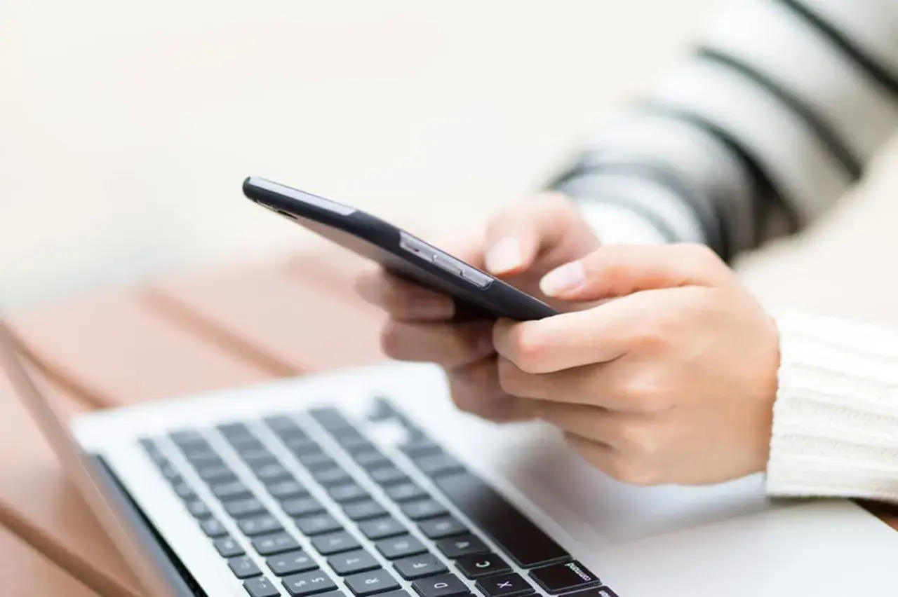 Mains tenant un smartphone, à côté d'un ordinateur portable. Une question se pose : que devient votre ancien numéro de téléphone ?