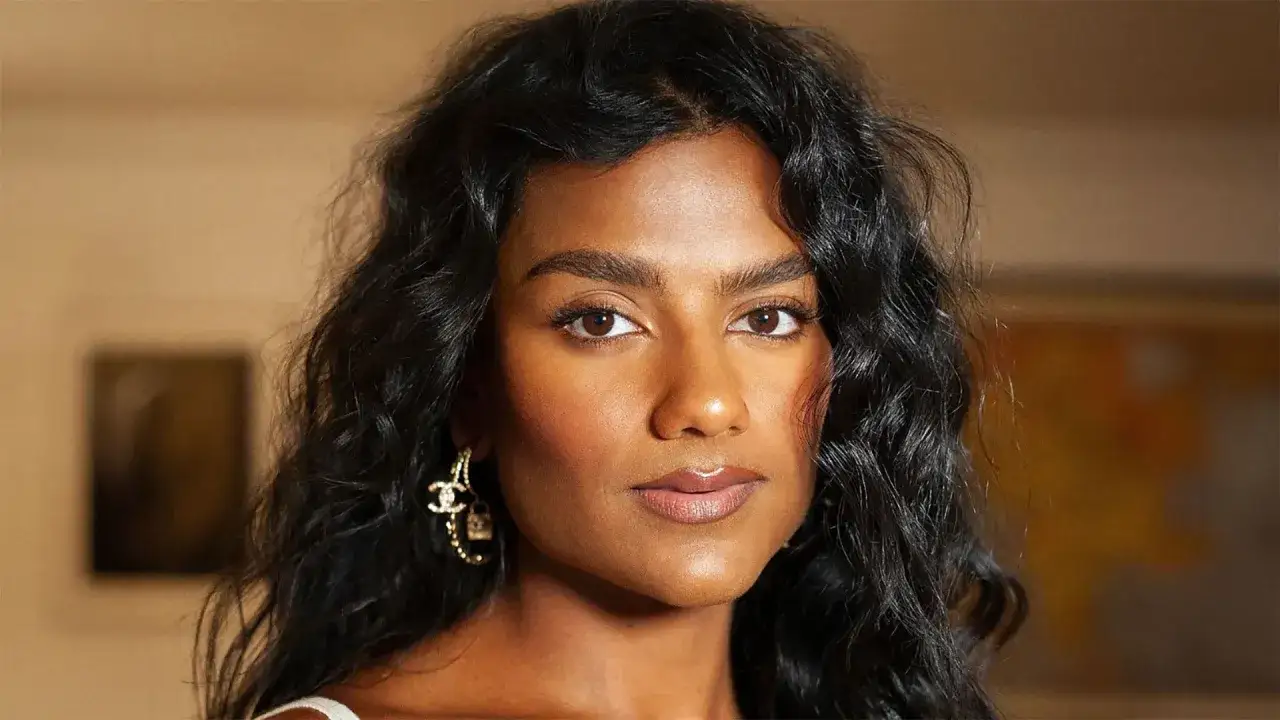 Mujer con pelo poco rizado y oscuro, luciendo unos pendientes dorados con el logo de Chanel.