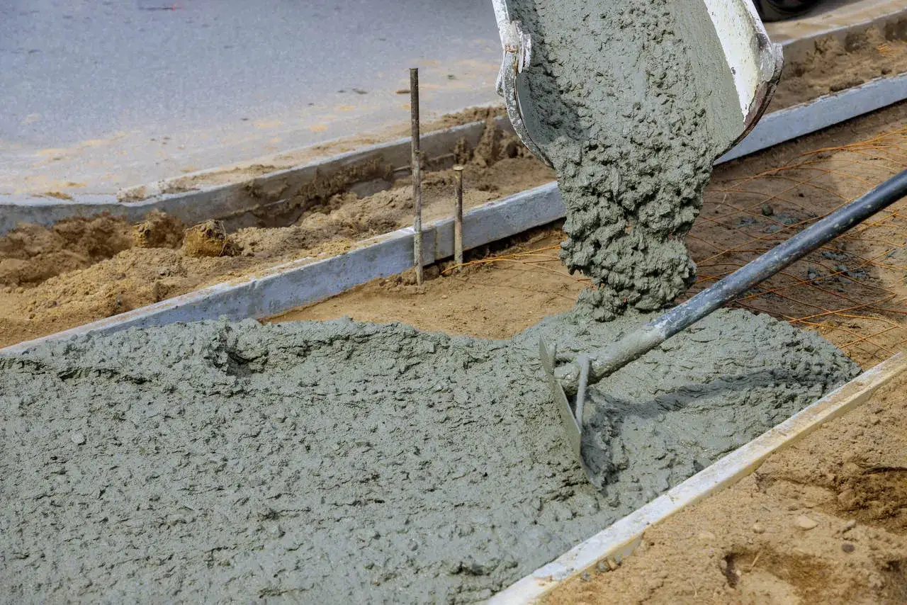 Wylewanie świeżego betonu na płytę fundamentową. Widać mieszankę, która spływa z gruszki, oraz narzędzia do jej rozprowadzania.