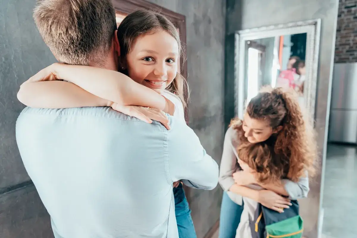 Uśmiechnięta dziewczynka mocno przytula tatę. W tle mama tuli synka, tworząc obraz silnej więzi rodzinnej, która wspiera psychikę wszystkich.