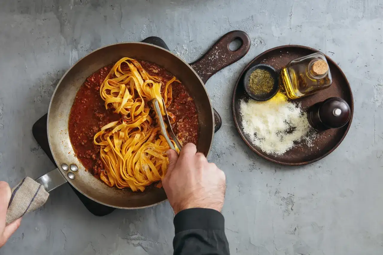 Jak ugotować makaron? W garnku sos boloński, a obok parmezan, oliwa i przyprawy. Gotowe do podania!