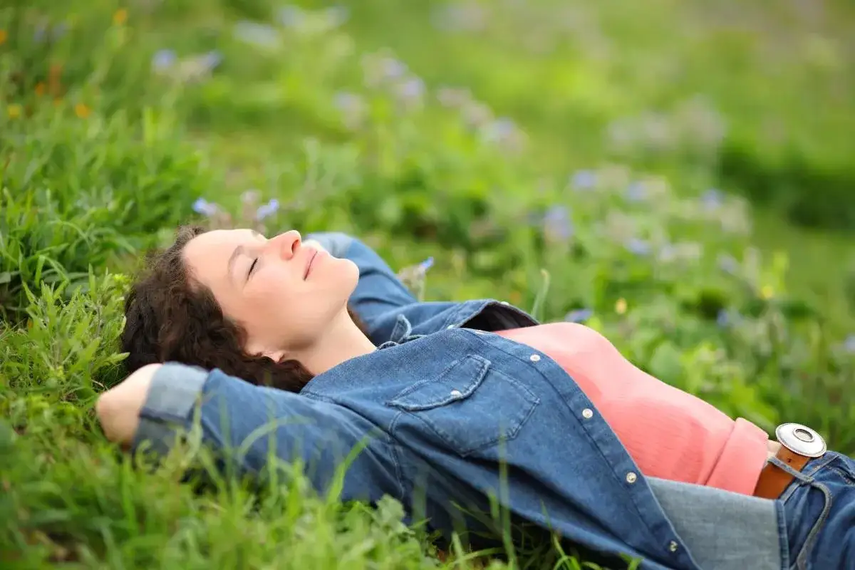 Mujer descansando en la hierba, sintiendo el poder femenino de la naturaleza y la paz interior.