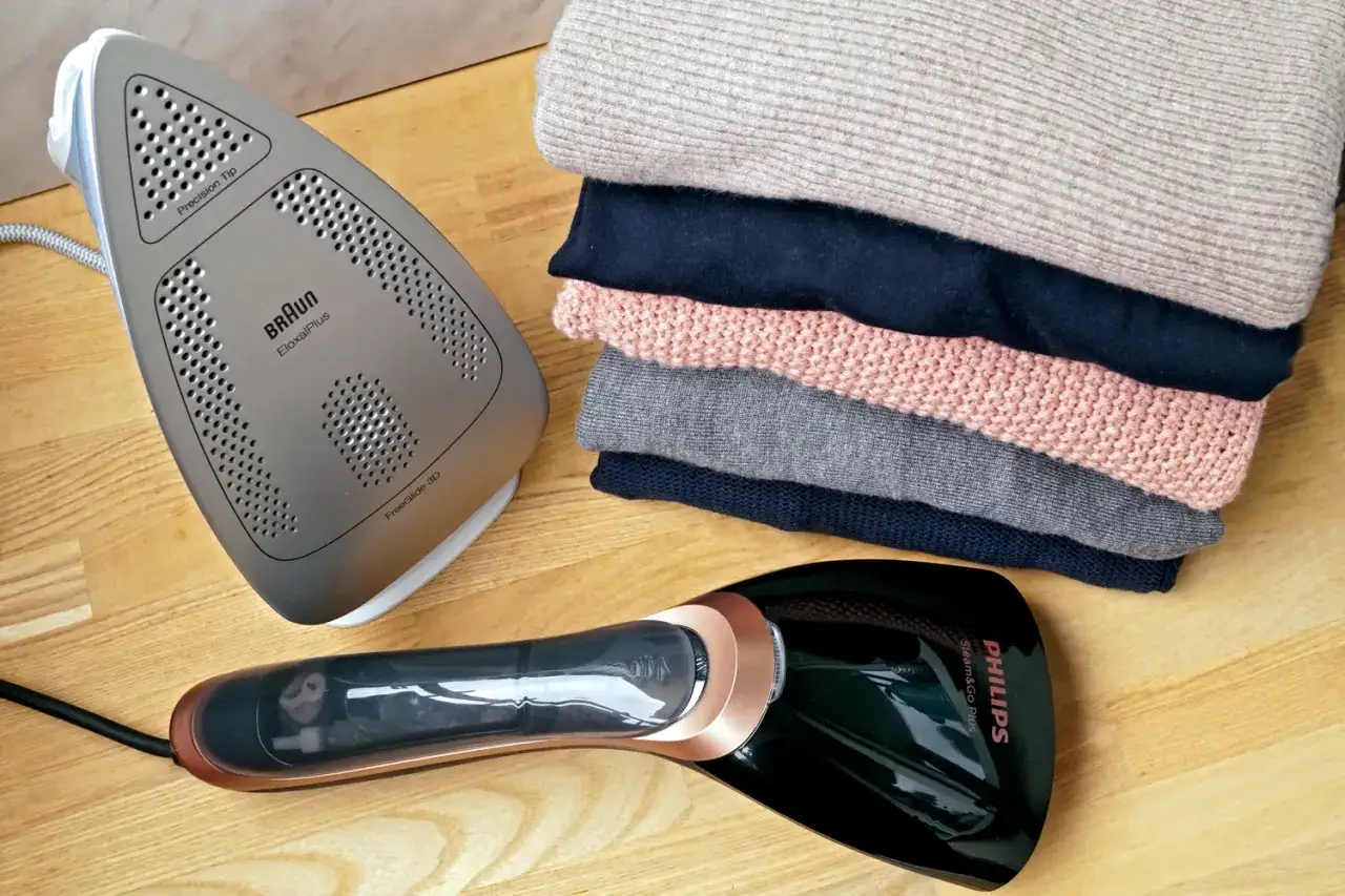 Parownica do ubrań Philips obok tradycyjnego żelazka Braun i stosu swetrów. Dlaczego parownice do ubrań stają się popularniejsze od tradycyjnych żelazek? Szybkość i wygoda!