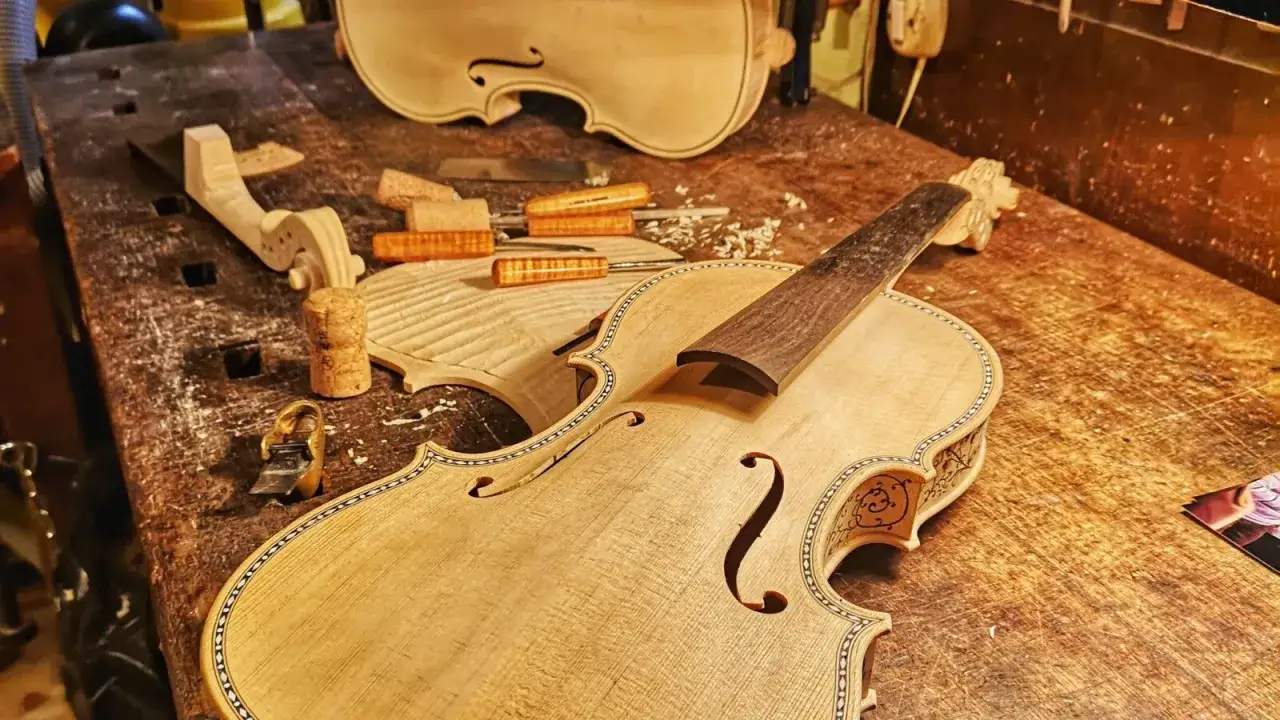 Il liutaio, con la sua arte, dà forma a strumenti musicali. In laboratorio, un violino in costruzione, con legni grezzi e attrezzi.