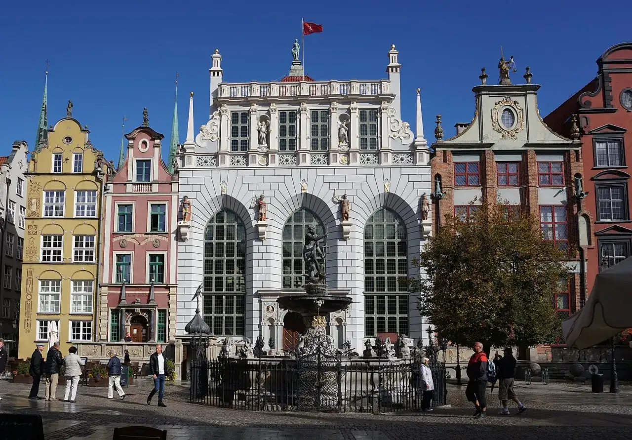 Neptunowa fontanna przed Artusowym Dworem w Gdańsku. W tle kolorowe kamienice i błękitne niebo.