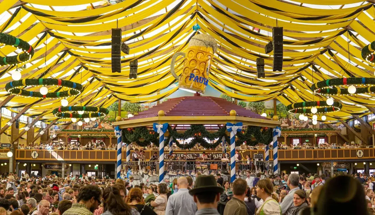 Folla festante sotto un tendone giallo e nero, con un'enorme boccale di birra che domina la scena. Atmosfera delle feste tedesche oktoberfest.