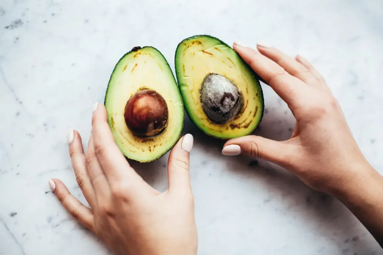Due mani accarezzano un avocado tagliato a metà, mostrando come si mangia l'avocado: un frutto cremoso pronto per essere gustato.