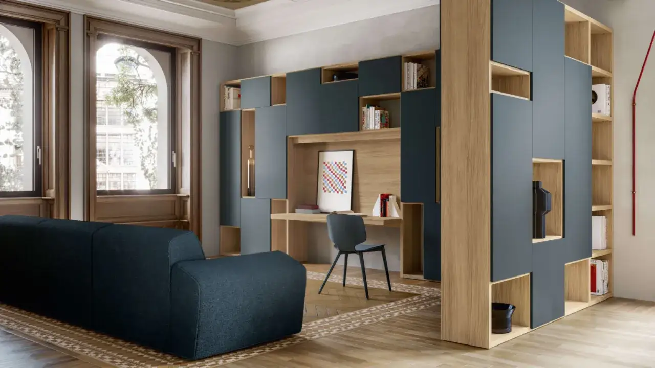 Un ampio soggiorno con un divano blu scuro e una libreria modulare che integra una scrivania. L'open space tv è al centro, incorniciato da elementi in legno e blu.