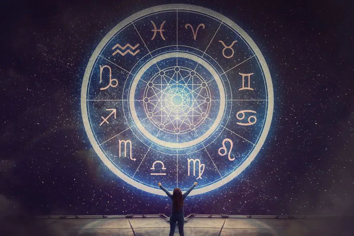 Osoba z rękami w górze patrzy na wielką tarczę zodiaku. Widać na niej znaki powietrzne: Bliźnięta, Waga, Wodnik.