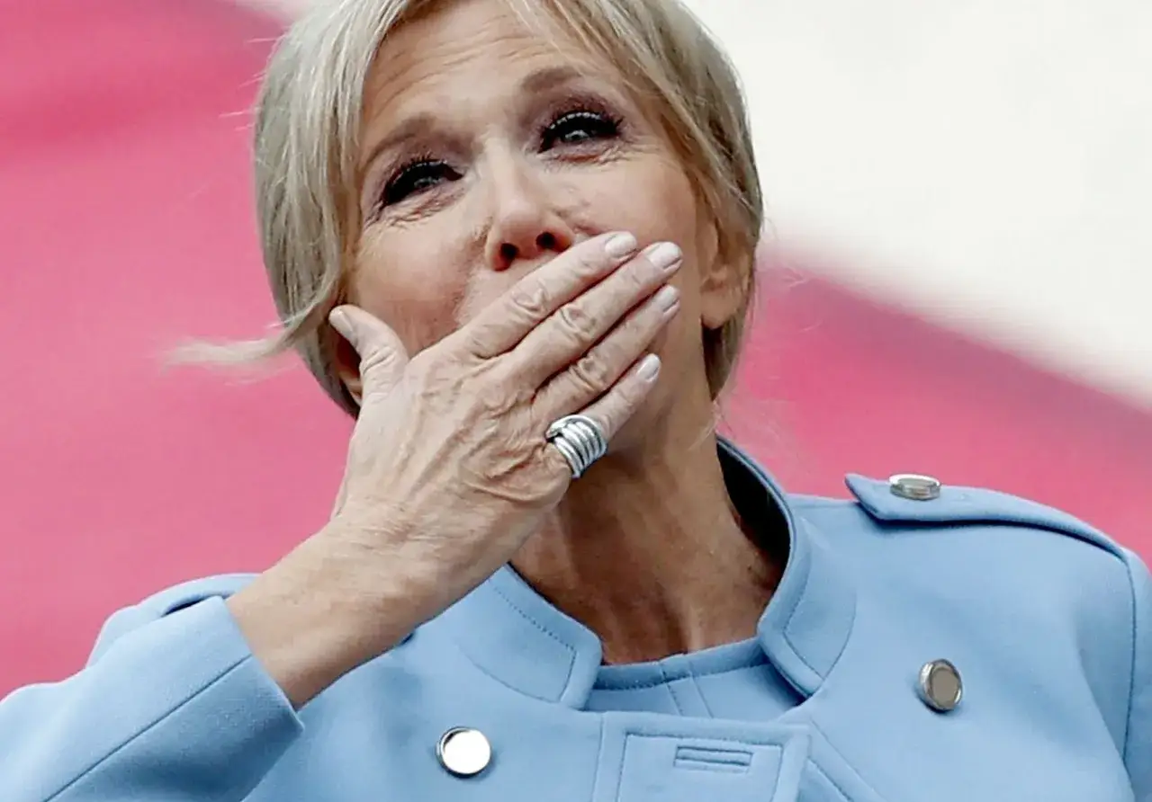 Brigitte Macron z dłońmi na ustach, jej jasne włosy lekko rozwiane.