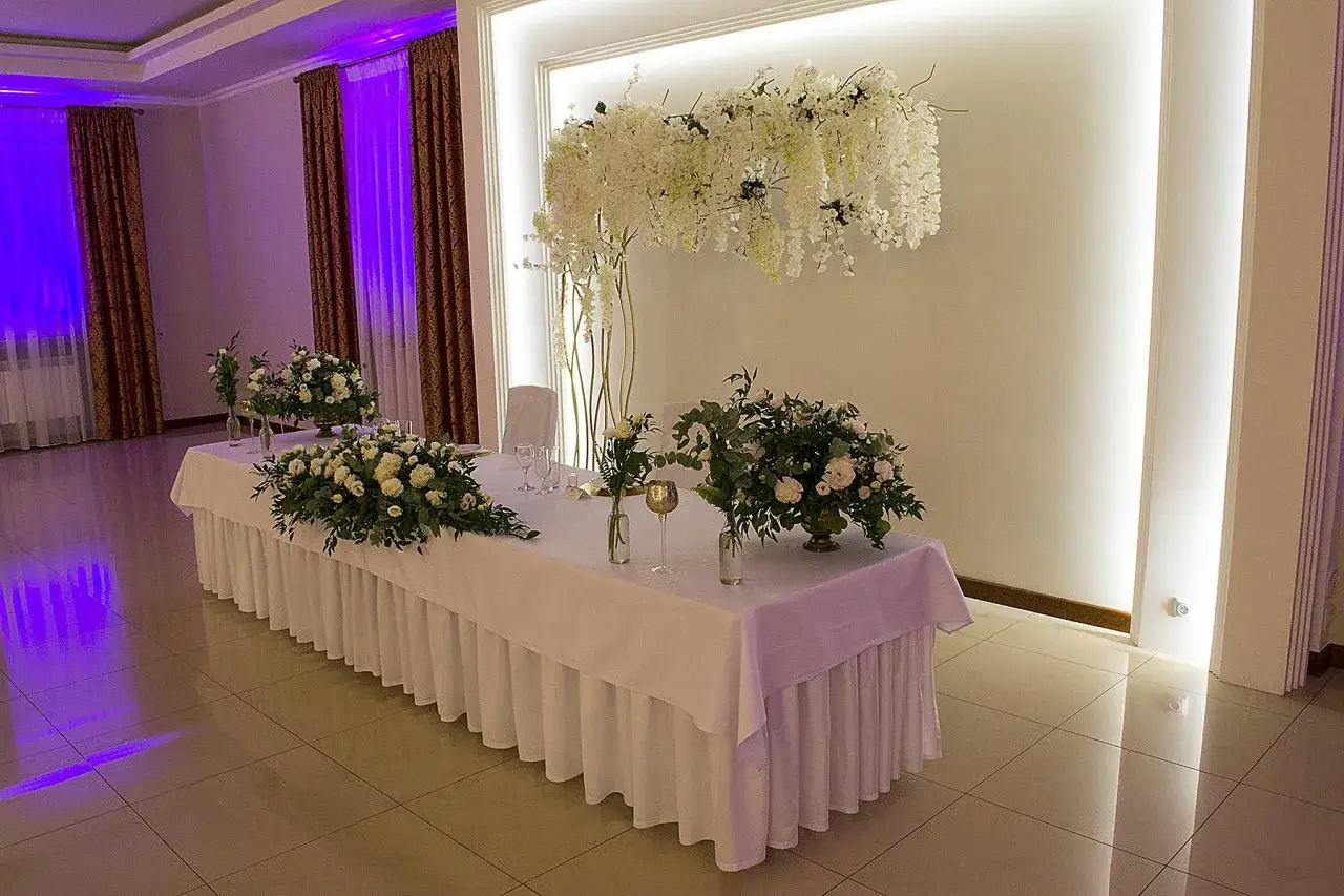 Elegancka sala weselna w Dworku Kasztelan Serokomla. Stół udekorowany białymi kwiatami i zielenią.