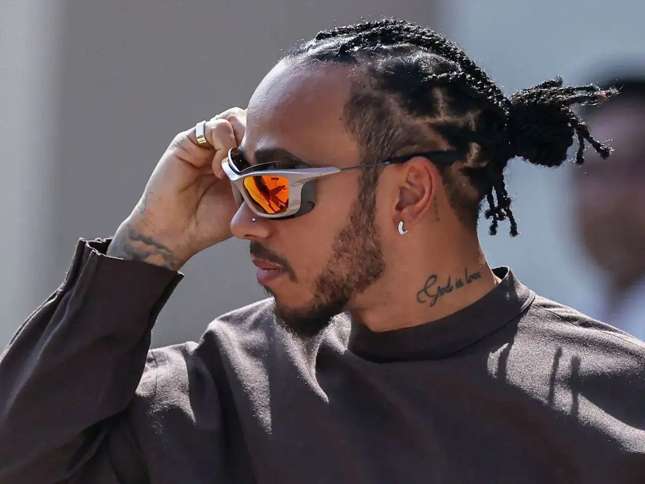 Mann mit geflochtenen Haaren und Bart, der eine trendige Sonnenbrille für Herren mit orangefarbenen Gläsern zurechtrückt.