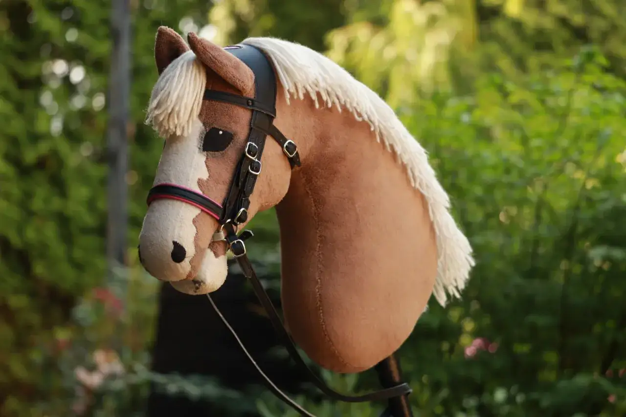 Brązowy koń na kiju z białym ogonem i grzywą, ubrany w czarne ogłowie dla hobby horse.