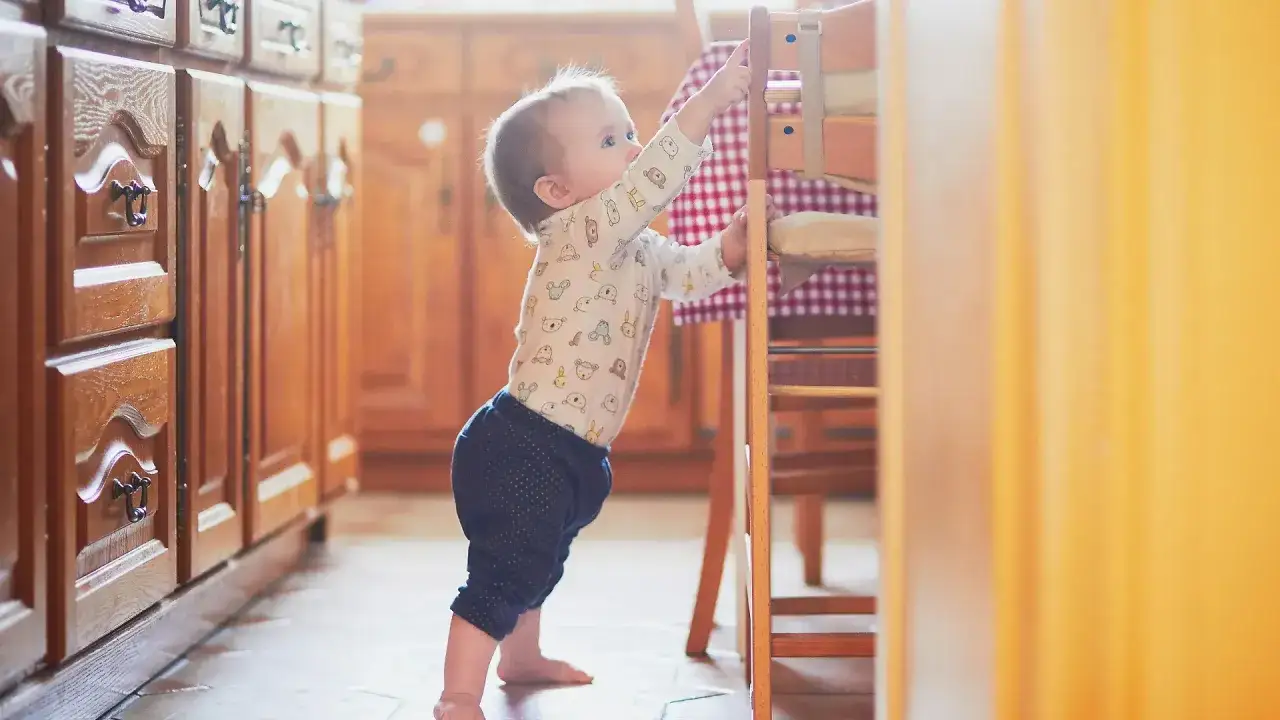 Kleines Baby zieht sich an einem Hochstuhl hoch. Ab wann ziehen sich Babys hoch? Dieses Baby ist auf dem besten Weg!