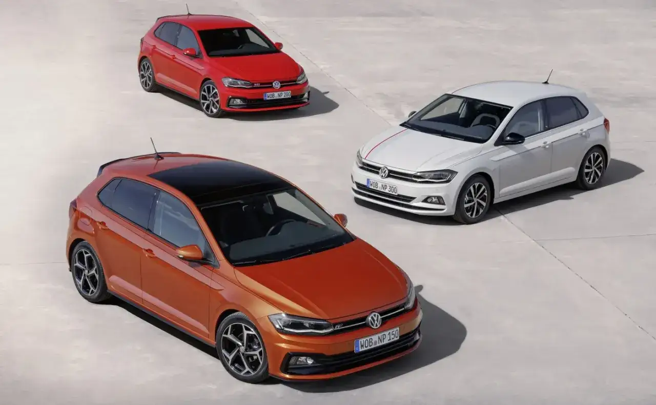 Trzy Volkswageny Polo 6R: pomarańczowy z czarnym dachem, czerwony i biały z czerwonymi pasami, stoją na betonowym placu.