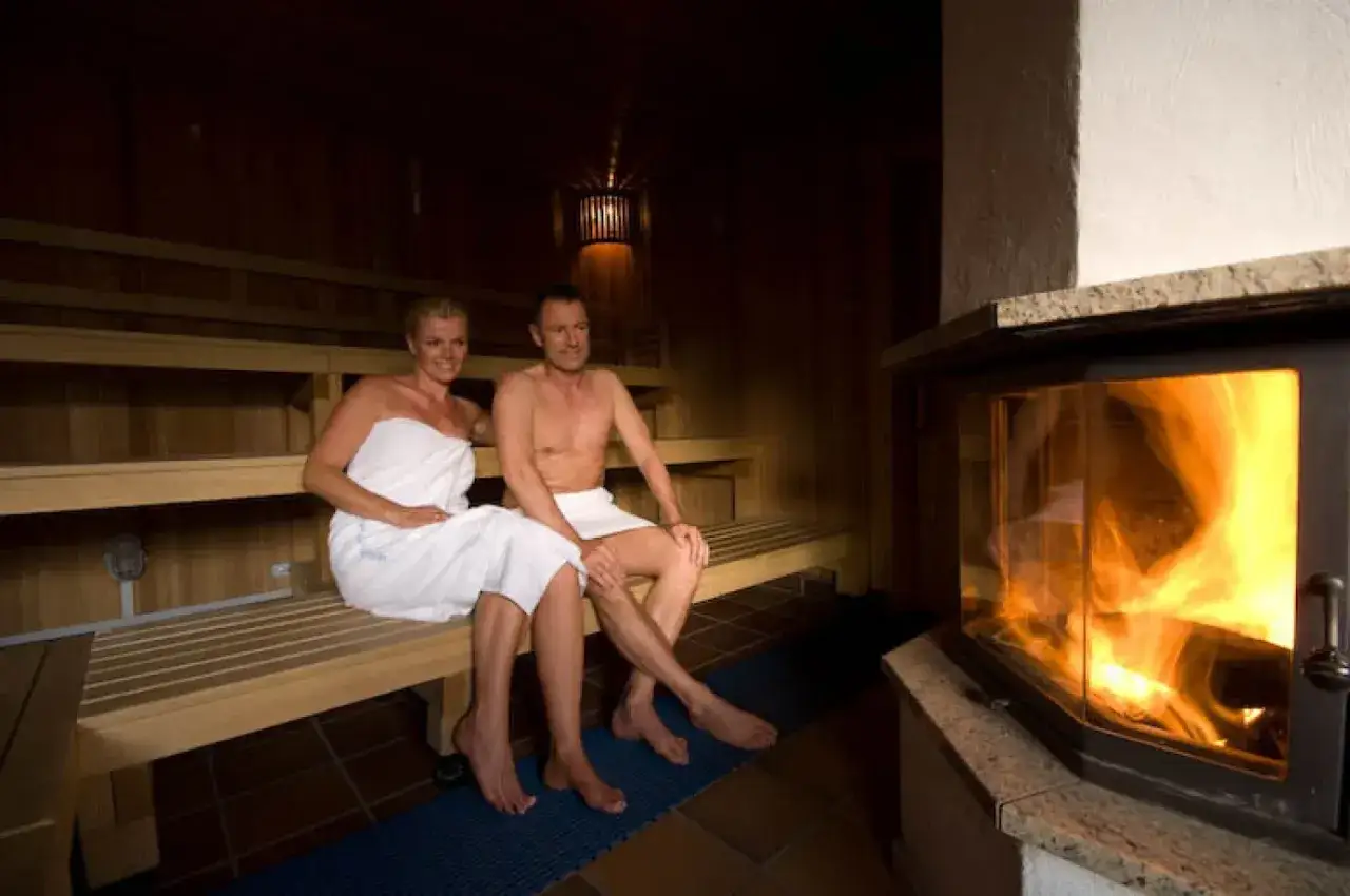 Ein Paar entspannt in der niederrhein therme mattlerbusch, umgeben von warmem Holz und dem Schein eines Kamins.
