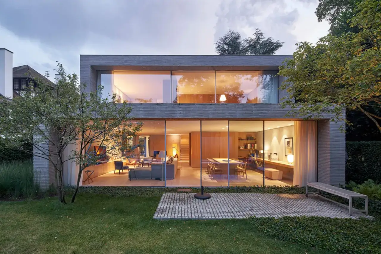 Modernes Haus mit Flachdach und bodentiefen Fenstern, die den Blick auf ein stilvolles Wohn- und Esszimmer freigeben.