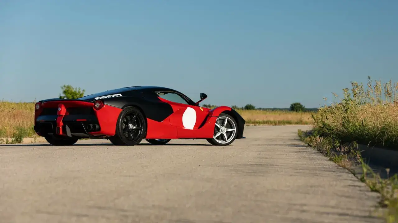 Czerwono-czarne Ferrari LaFerrari z białymi okręgami na drzwiach, stojące na pustej drodze. Zastanawiasz się, ile kosztuje Ferrari LaFerrari?