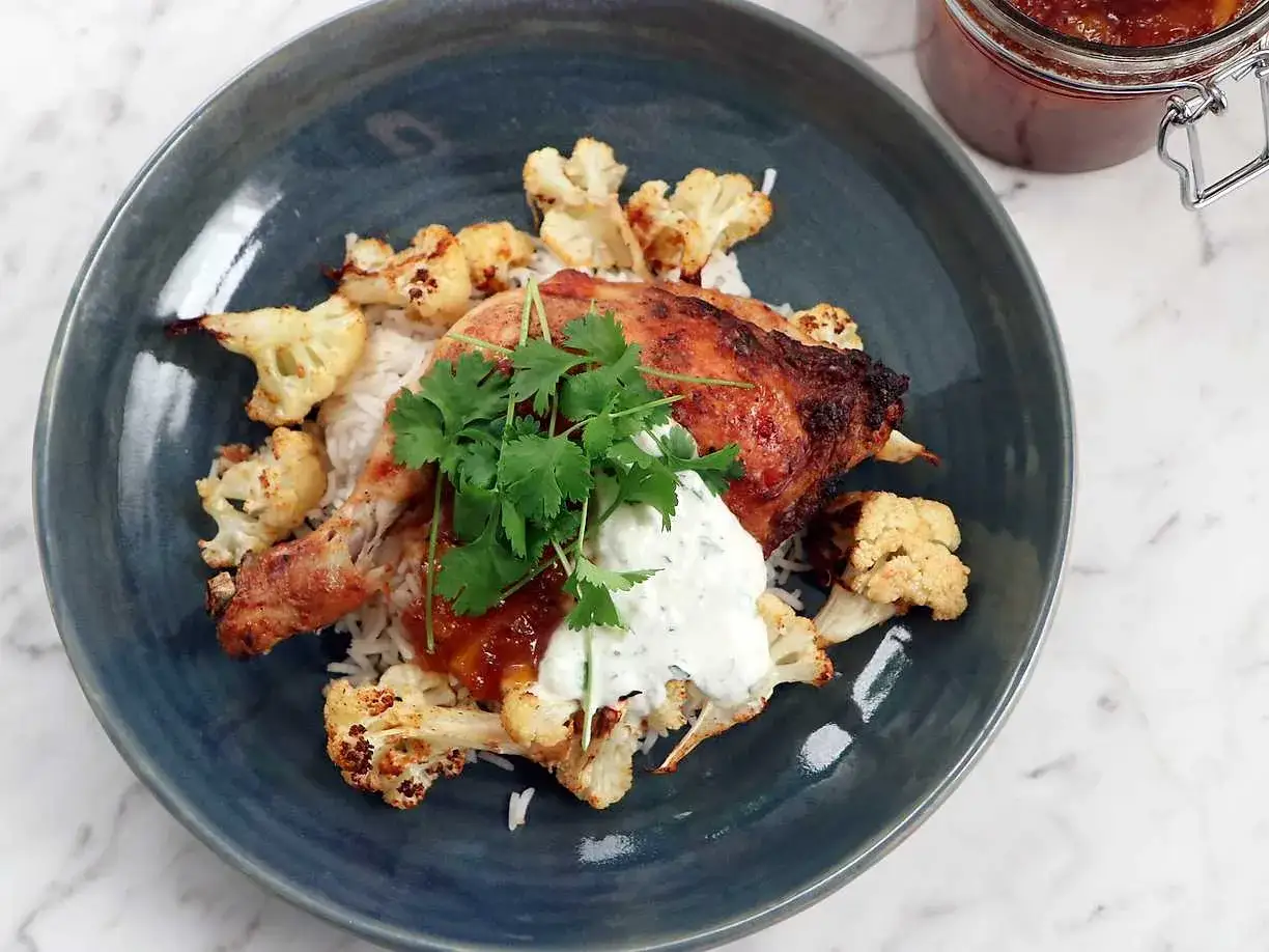 En tallrik med ris, tandoori kyckling, blomkål och en klick vit sås. Perfekt för ett tandoori kyckling recept!