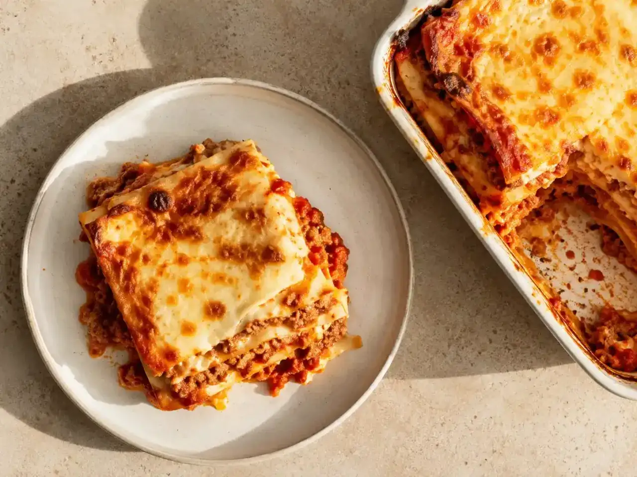En härlig glutenfri lasagne med gyllene ost och rikligt med köttfärssås. En portion ligger på en tallrik bredvid formen.