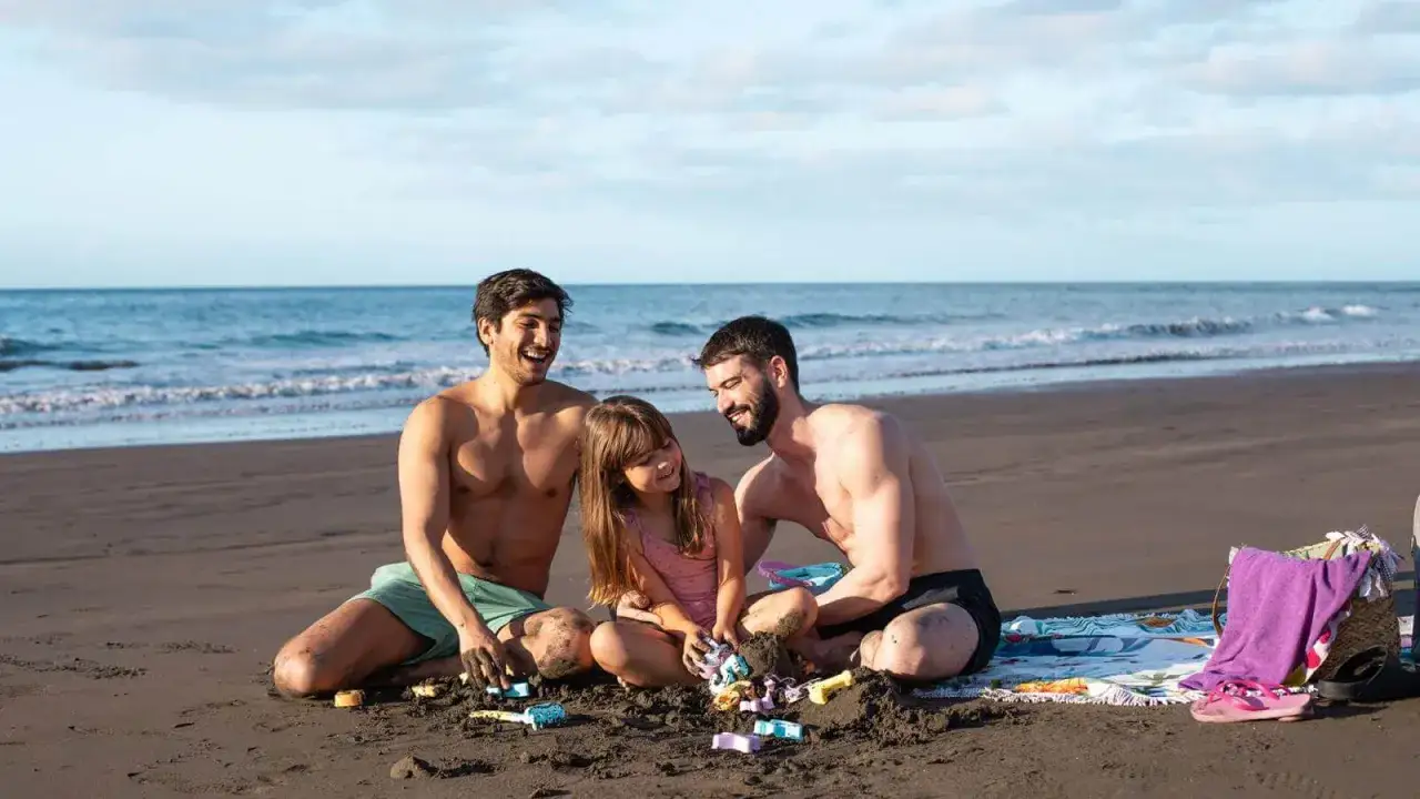 A happy family enjoys a day at the beach in the Canary Islands. Two men and a young girl build sandcastles, their laughter echoing over the waves.