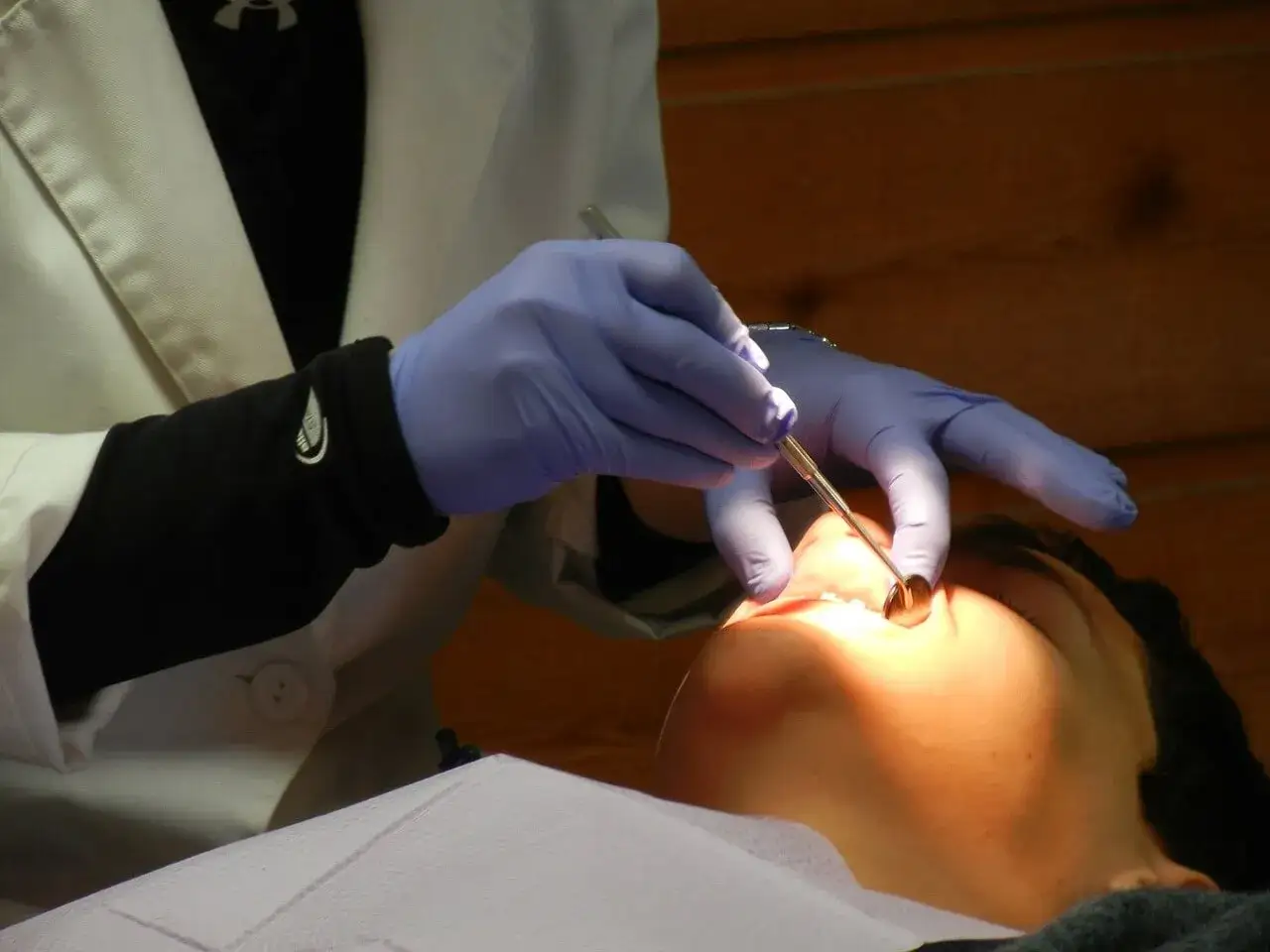 Dentysta w niebieskich rękawiczkach bada ząb pacjenta lusterkiem. Czy to już czas na plombę?