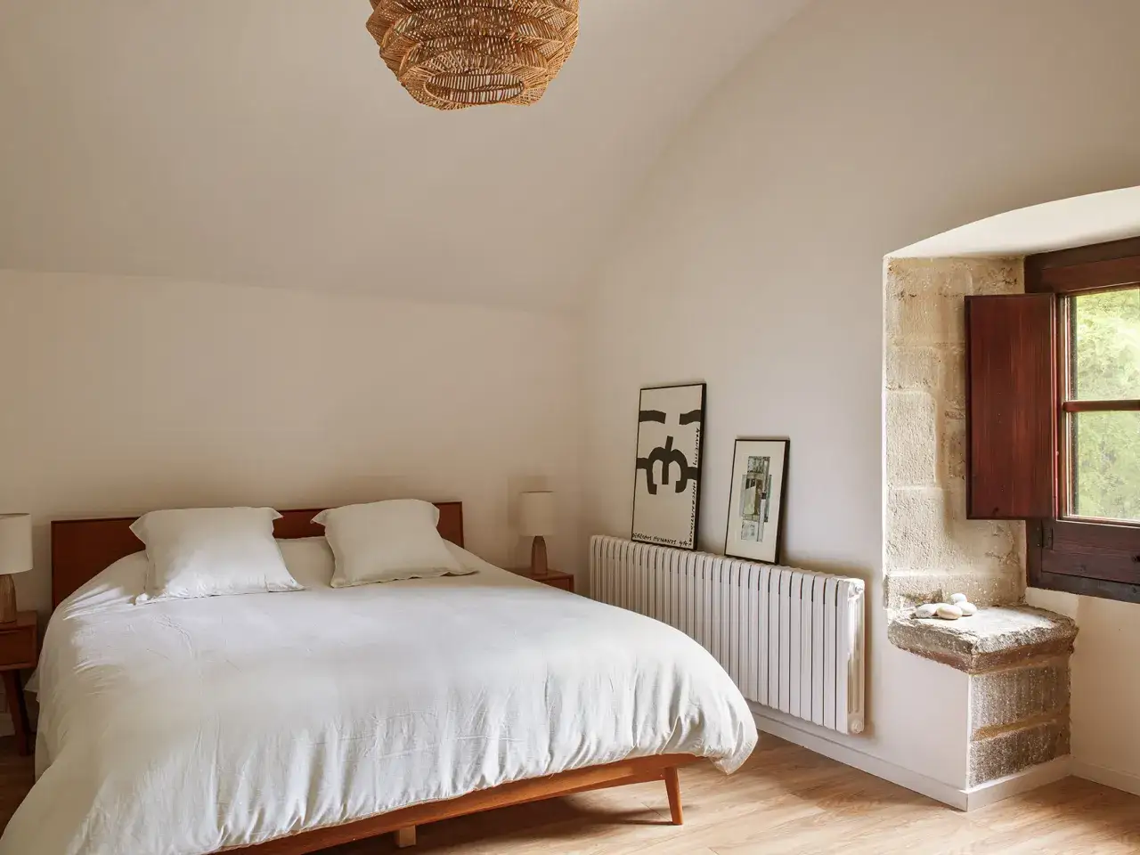 Habitaci&oacute;n con cama blanca y radiador. Abre la ventana para refrescar la habitaci&oacute;n y disfrutar de la luz natural.