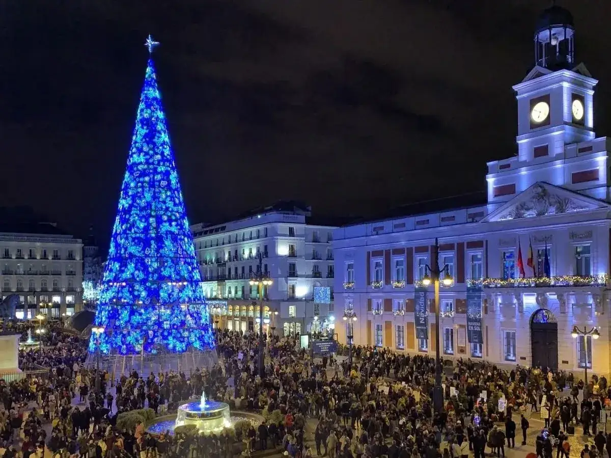 Una multitud celebra la Navidad en la Puerta del Sol de Madrid, bajo un árbol gigante iluminado de azul. ¡Excelentes planes de Navidad en Madrid!