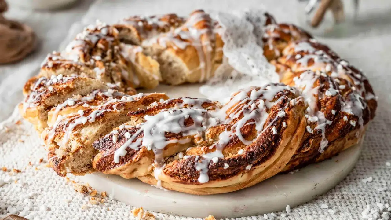 Ein goldbrauner nusskranz hefe, mit Zuckerguss und Hagelzucker bestreut, liegt auf einem Marmorsockel.