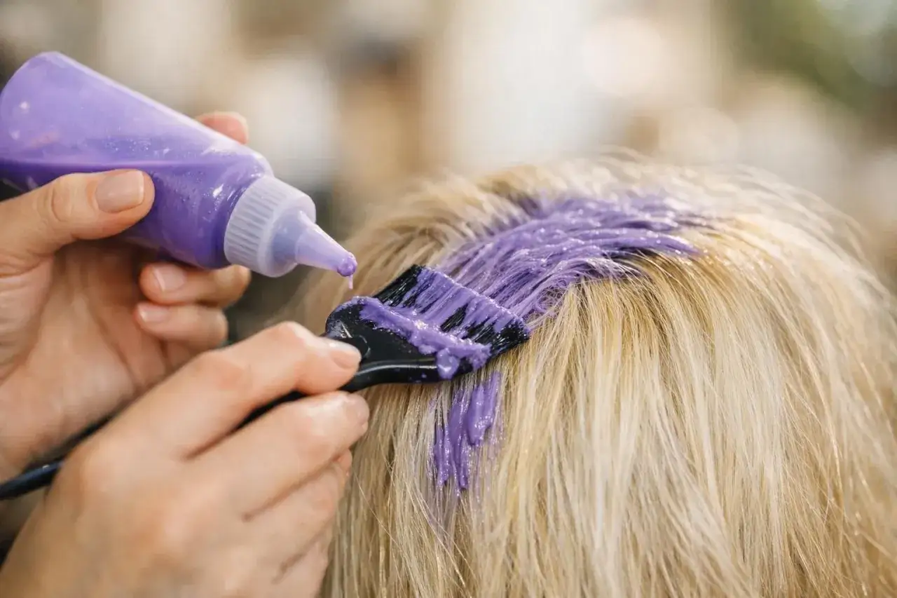 Application d'une patine violette sur des cheveux blonds pour neutraliser les reflets jaunes.