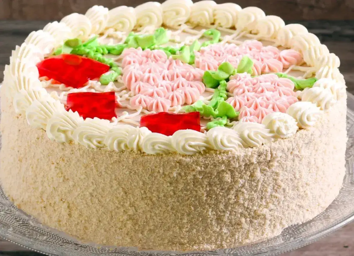 Tort ozdobiony kremem, różowymi kwiatkami i galaretką. W środku puszysta masa budyniowa z mascarpone.