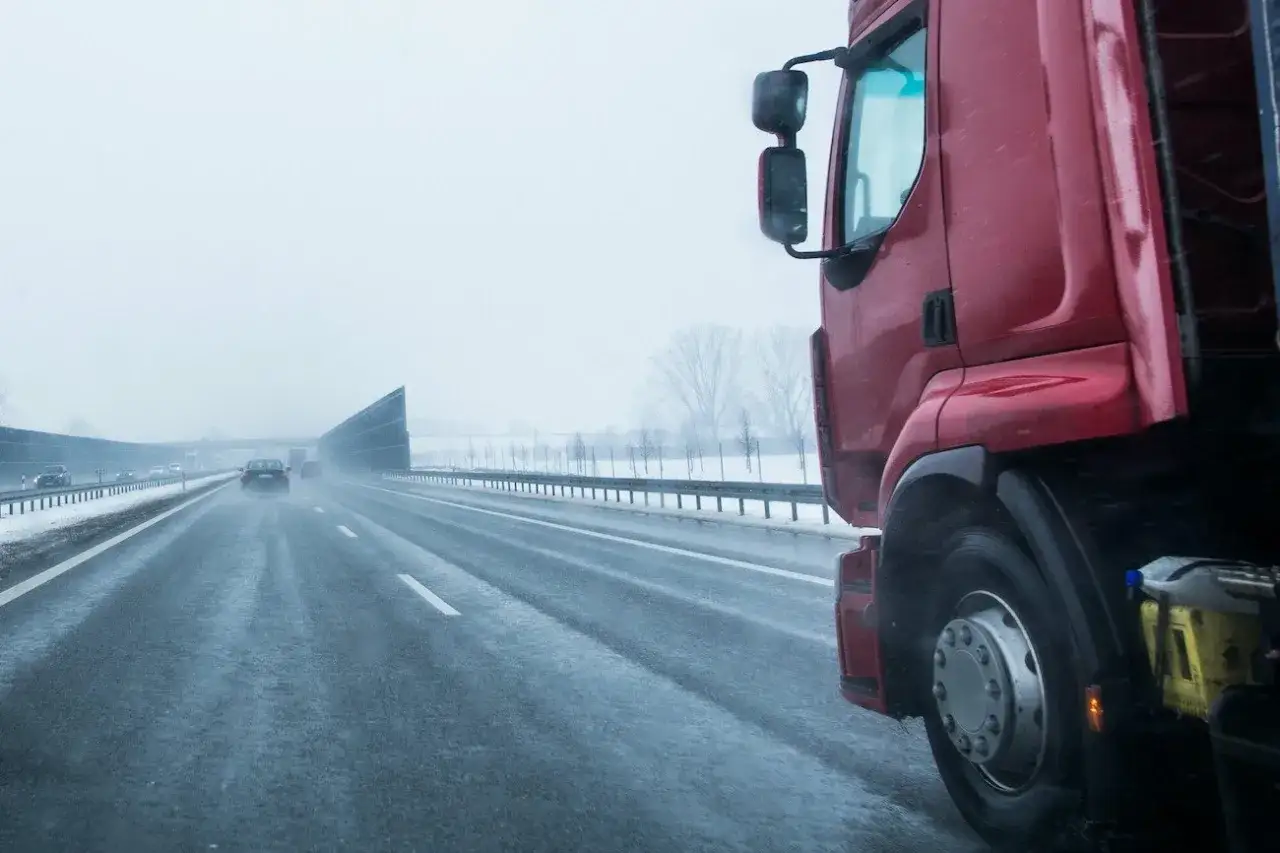 Czerwony tir na mokrej autostradzie w zimowy dzień. Kierowcy ciężarówek w Polsce zarabiają różnie, zależnie od doświadczenia i trasy.