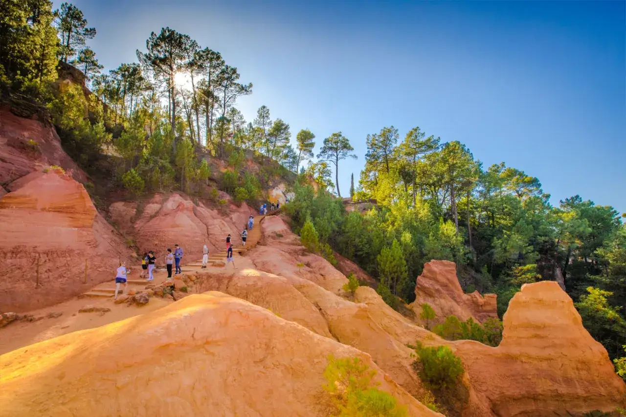 Des randonneurs explorent le sentier des ocres, un paysage spectaculaire aux teintes orang&eacute;es et rouges, typique du Colorado proven&ccedil;al.